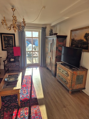 A living room with a television, a patterned rug, a wooden cabinet, and a chandelier. - Garden Villa Schwanstein I Apartment "Leda" with roof terrace (Füssen)