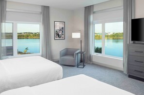 A hotel room with two beds, a desk, a chair, a TV, and large windows with a view of a body of water and greenery. - Residence Inn by Marriott Portland Thompson's Point (Portland)