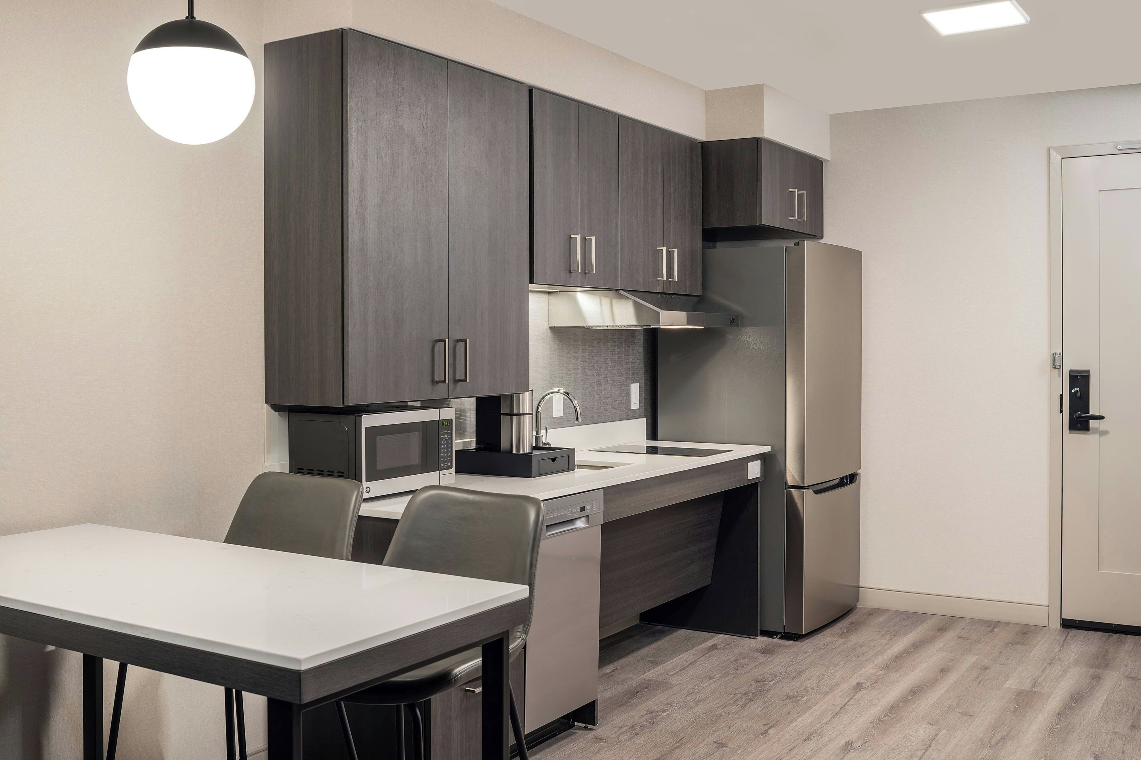 A compact kitchen with dark cabinets, a stainless steel refrigerator, a microwave, and a dining area with a table and chairs.