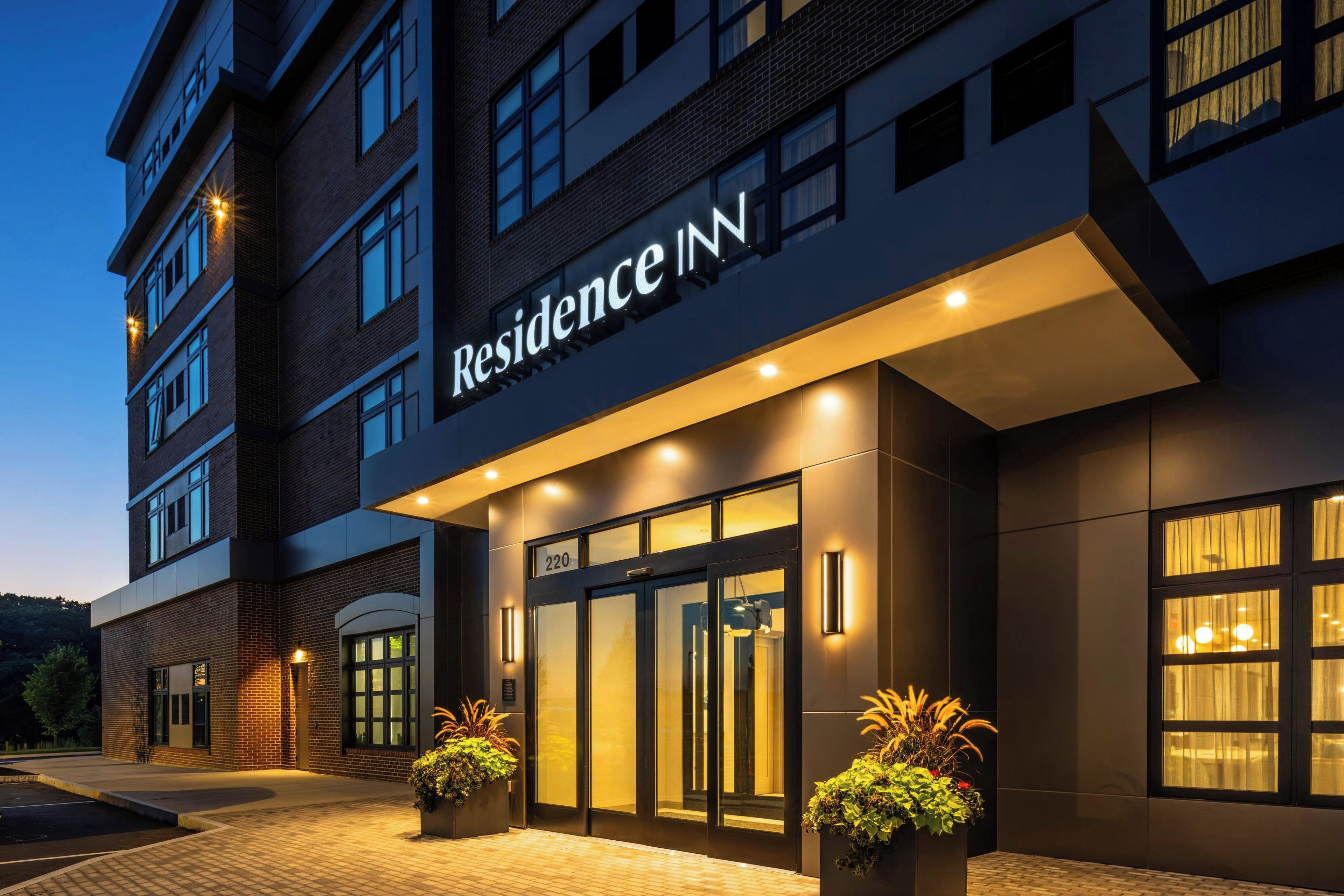 Ein Hotel Eingang mit einem 'Residence Inn' Schild, einem schmiedeeisernen Tor und zwei Blumentöpfen.