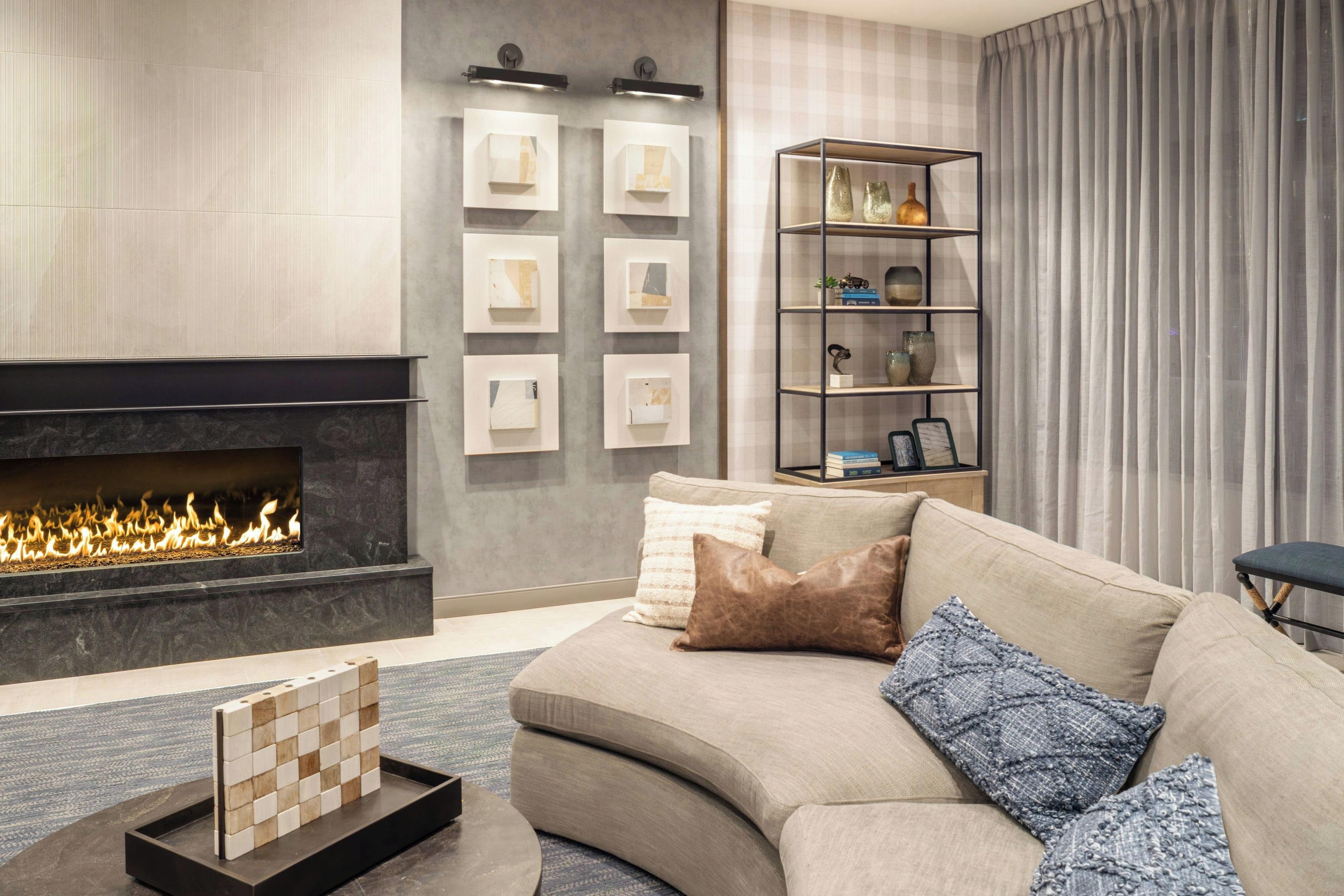 A modern living room with a fireplace, a sofa with cushions, a bookshelf, and framed artwork on the wall.
