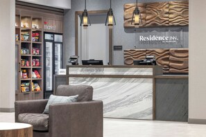 A hotel reception area with a marble counter, a seating area with a sofa and armchair, and a wall-mounted clock. - Residence Inn by Marriott Portland Thompson's Point (Portland)