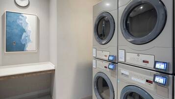 A laundry facility with multiple washing machines, a clock on the wall, and a framed artwork.