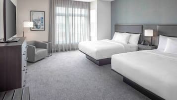 A hotel room with two beds, a desk, a chair, a television, and a window with curtains.