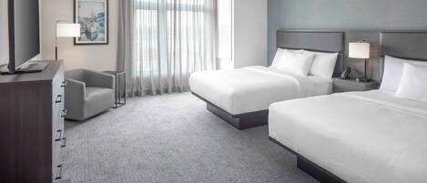Une chambre d’hôtel avec deux lits, un bureau, une chaise, une télévision et une fenêtre avec des rideaux.