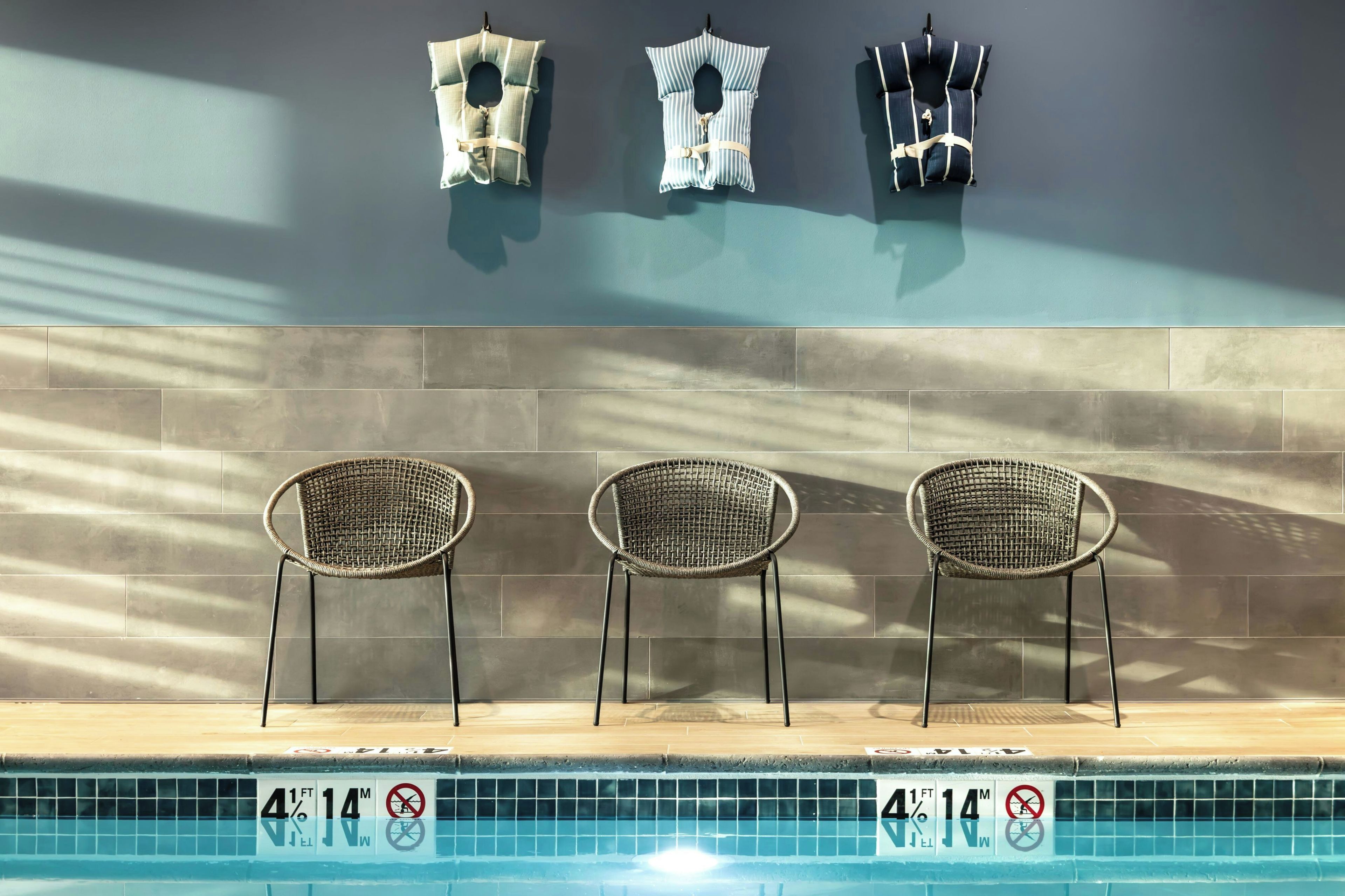 Área da piscina com três cadeiras de vime e três coletes salva-vidas na parede.