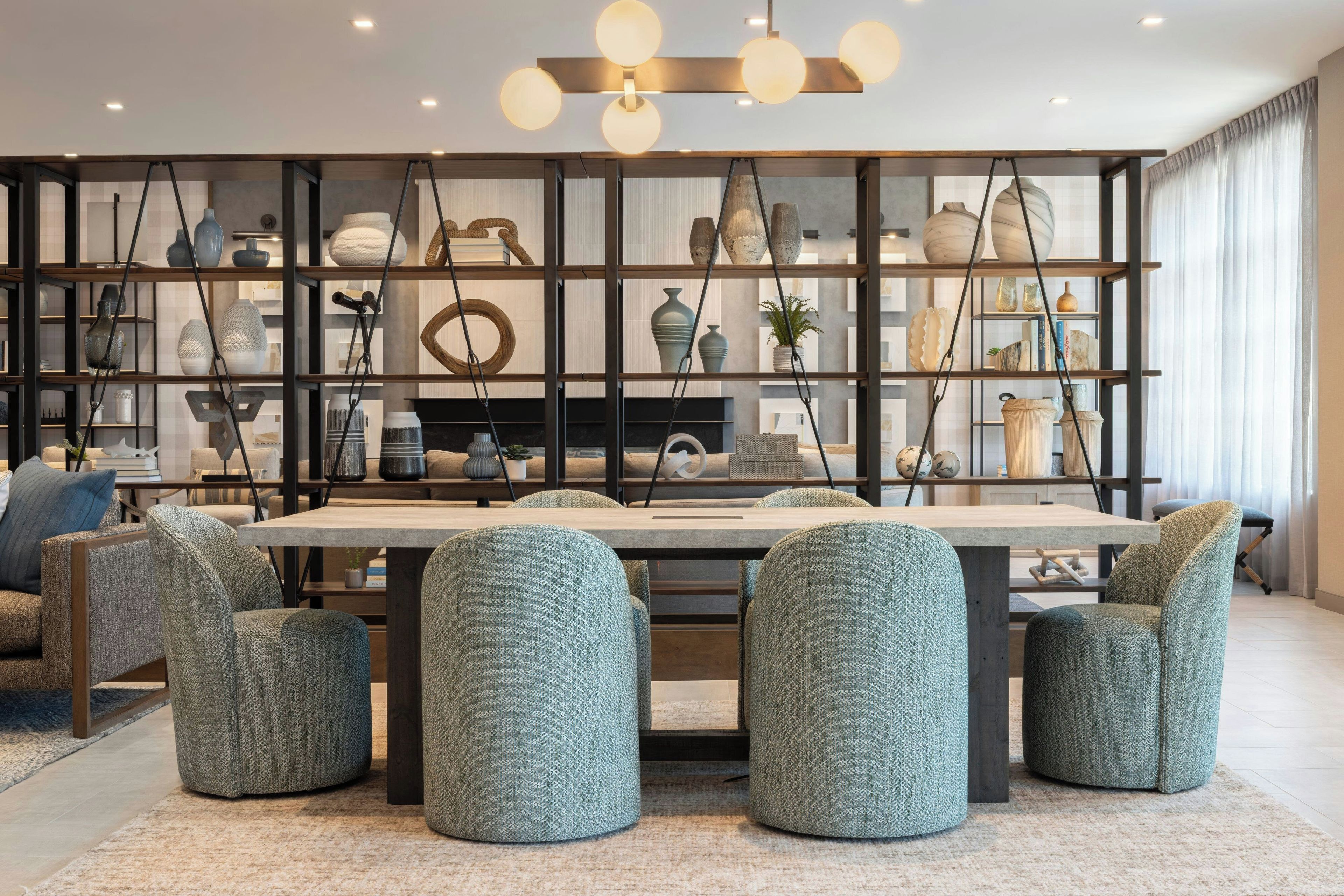 A modern dining area with a central table, surrounded by upholstered chairs, and a decorative wall with shelves displaying various items.