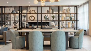 A modern dining area with a central table, surrounded by upholstered chairs, and a decorative wall with shelves displaying various items.