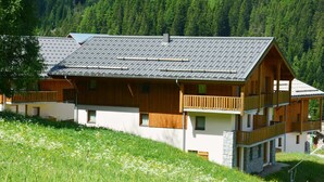 A two-story wooden chalet with balconies, set on a hillside with a forest backdrop. - Alpine Apartment Near Slopes (Modane)