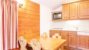 A wooden-paneled kitchen with a microwave, wooden cabinets, and a dining table with chairs. - Alpine Apartment Near Slopes (Modane)