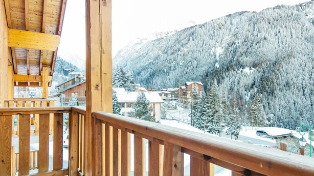 A wooden balcony with a view of a snowy mountain and buildings. - Alpine Apartment Near Slopes (Modane)