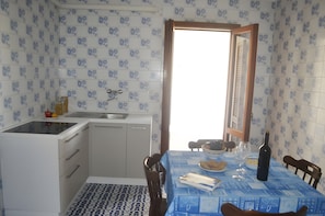 Cozinha compacta com armários brancos, pia e área de jantar com mesa posta para dois.