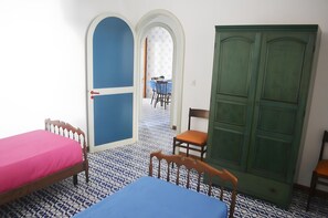 Quarto com duas camas, um guarda-roupa verde, uma mesa de jantar com cadeiras e chão estampado.
