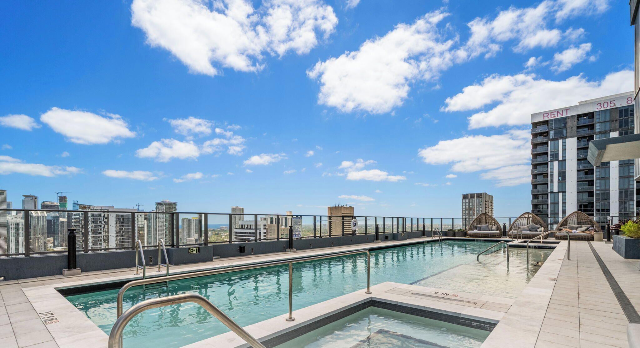 A rooftop pool with a city view, a sign indicating 'RENT 305', and a building with balconies.