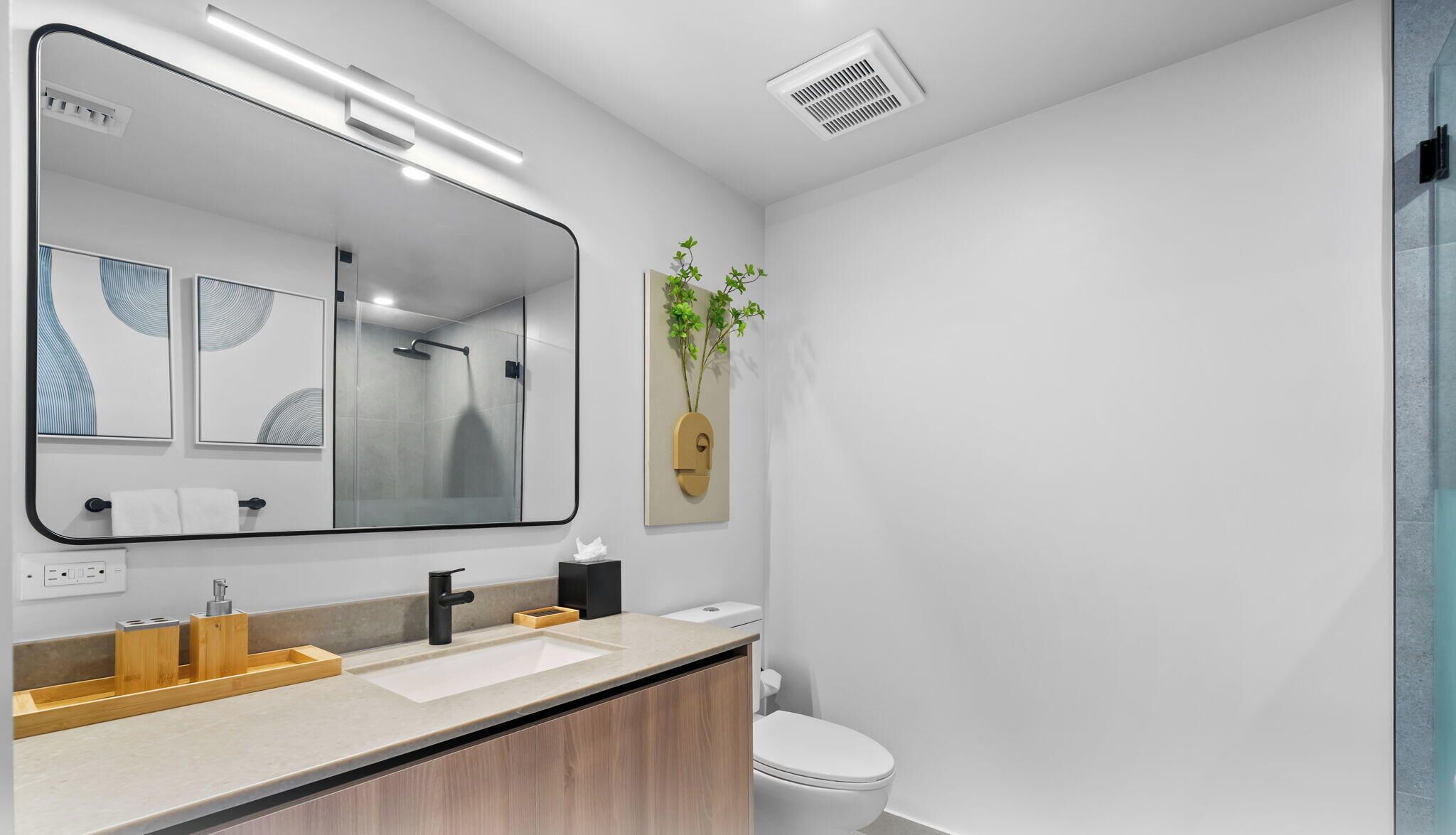 Une salle de bain moderne avec un grand miroir, une douche, des toilettes et un lavabo agrémenté d’accessoires en bois.