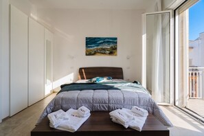 Een moderne slaapkamer met een groot bed, een schilderij aan de muur en uitzicht door een glazen schuifdeur.
