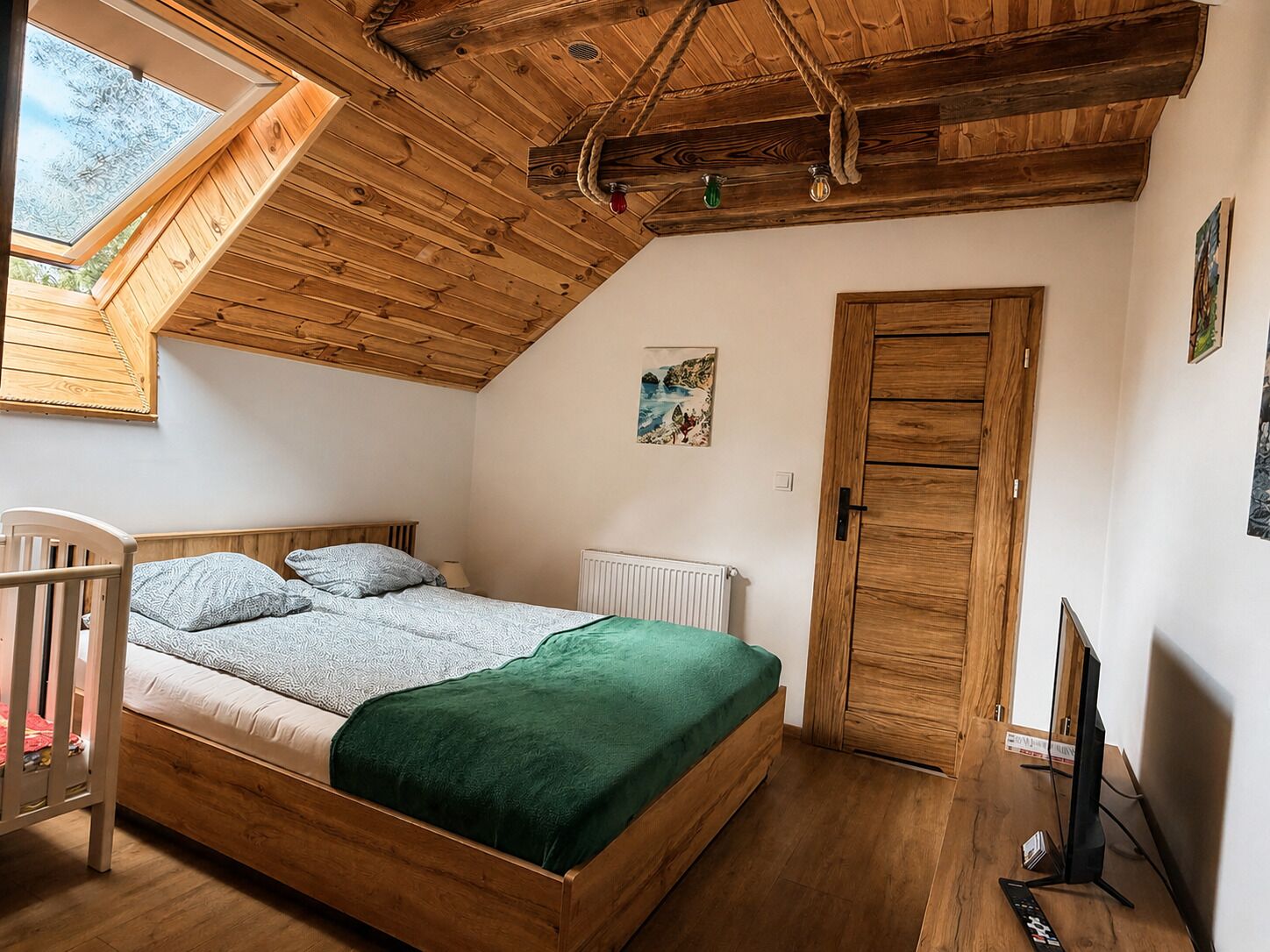 A bedroom with a sloped ceiling, a bed, a window, a door, and a television.