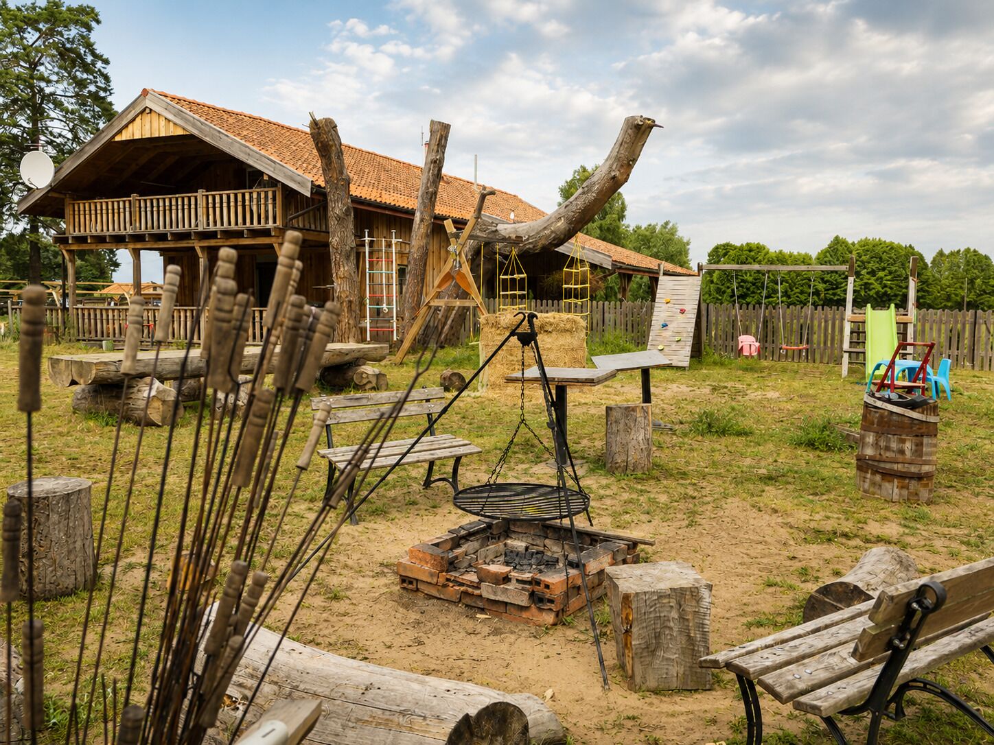A rustic outdoor setting with a wooden building, a fire pit, and various wooden structures.