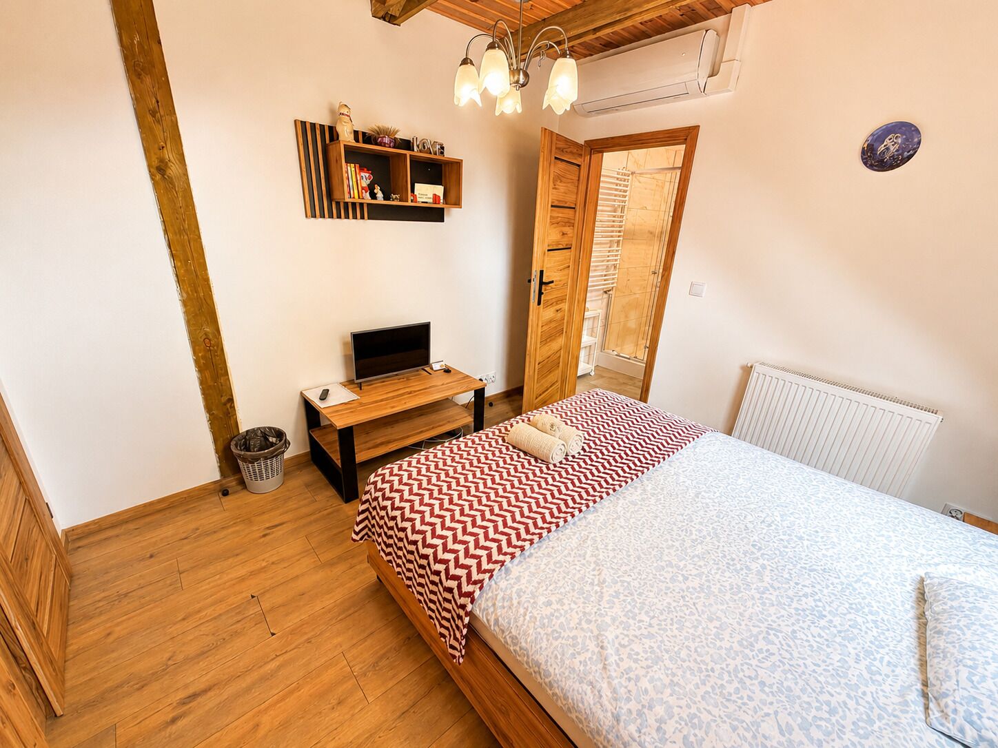 Un dormitorio con cama de madera, un escritorio con televisor, una estantería con libros y un letrero que dice 'LOVE'.