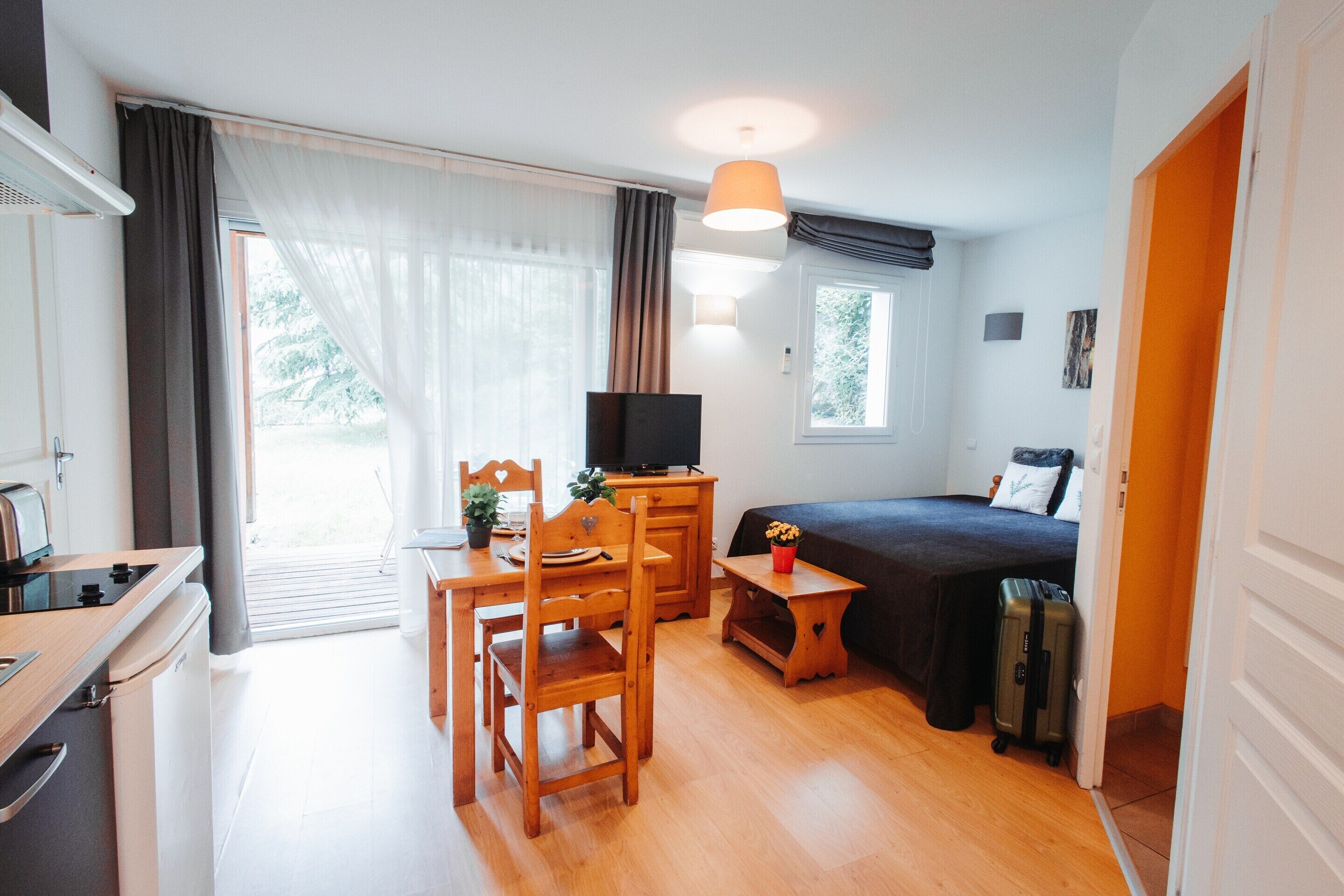 A room with a bed, a desk with a chair, a television, and a window with curtains.