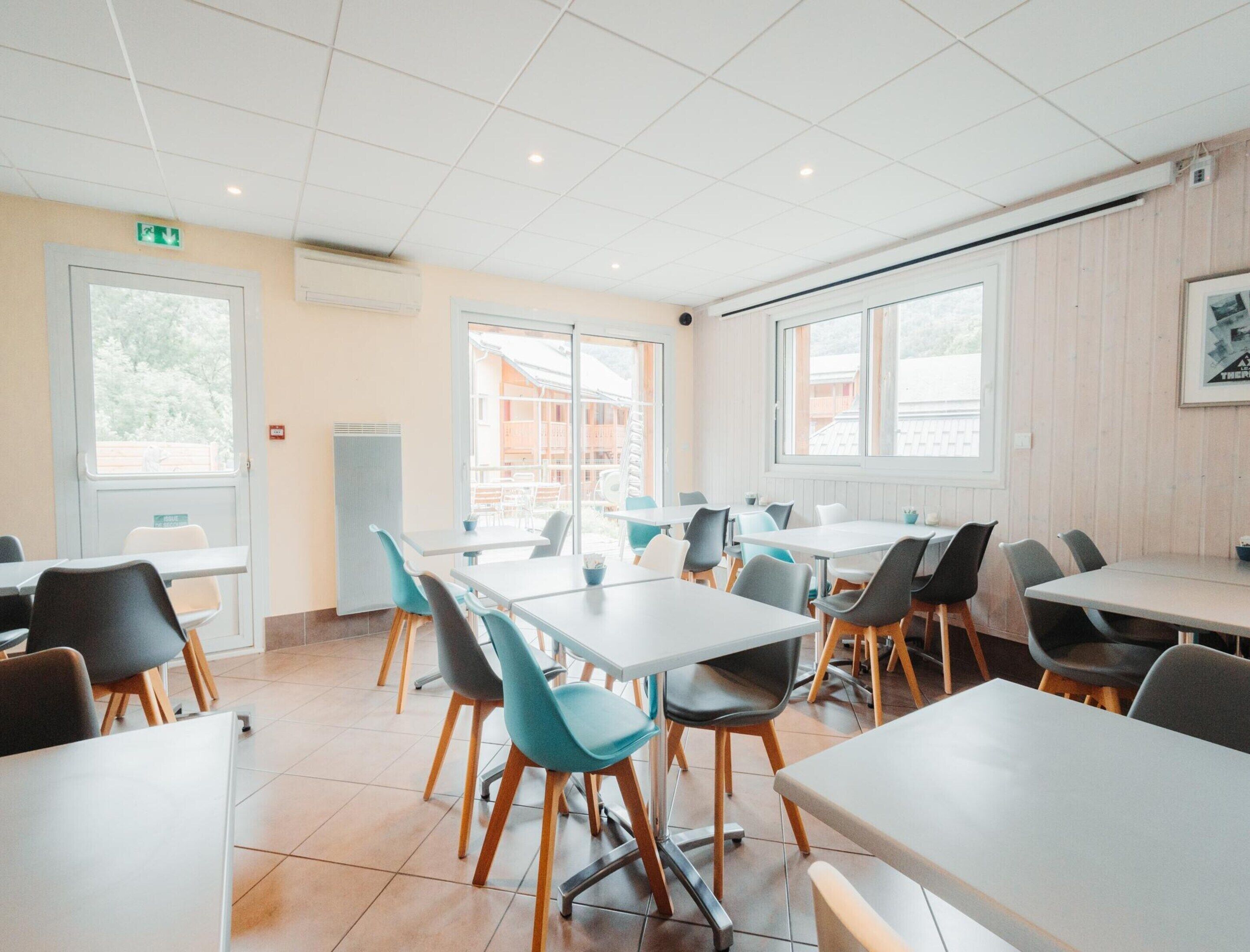 A dining area with tables and chairs, large windows, and a door with an emergency exit sign.