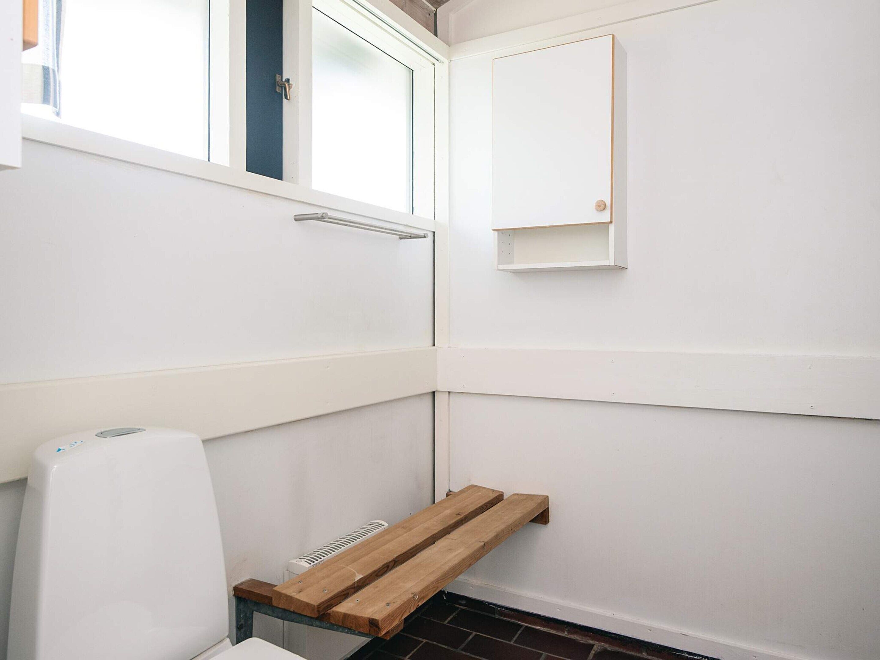 A bathroom with a white toilet, a wooden bench, a towel rack, and a medicine cabinet.