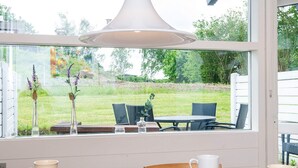 Ein Essbereich mit Tisch, Stühlen und Blick auf einen Garten durch große Fenster.