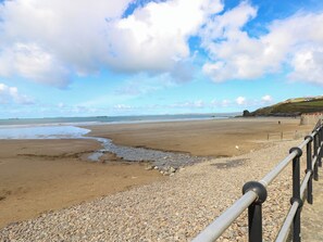 A beach with a pebble path, a railing, and a distant ship. - 8 Millmoor Farm Cottage (Haverfordwest)