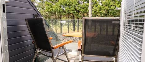 A patio with two chairs, a table, and a view of a forested area.