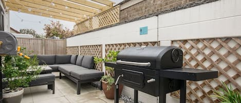 A patio with a barbecue grill, a sofa, and potted plants.