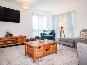 A living room with a wooden coffee table, a blue armchair, a grey sofa, a wooden side table, and a floor lamp. - Seagull Shack (Porthmadog)