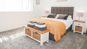 A bedroom with a bed, bedside tables, a bench with towels, a window, and a wall-mounted picture. - Seagull Shack (Porthmadog)