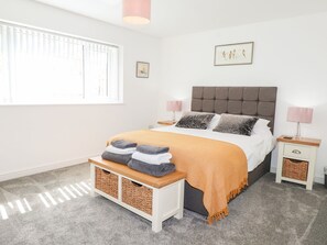 A bedroom with a bed, bedside tables, a bench with towels, a window, and a wall-mounted picture. - Seagull Shack (Porthmadog)