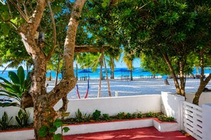 Blick auf einen Strand mit Palmen, einer weißen Wand und einem roten Teppich.