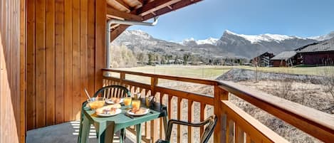 A wooden balcony with a table set for breakfast, overlooking snow-capped mountains.