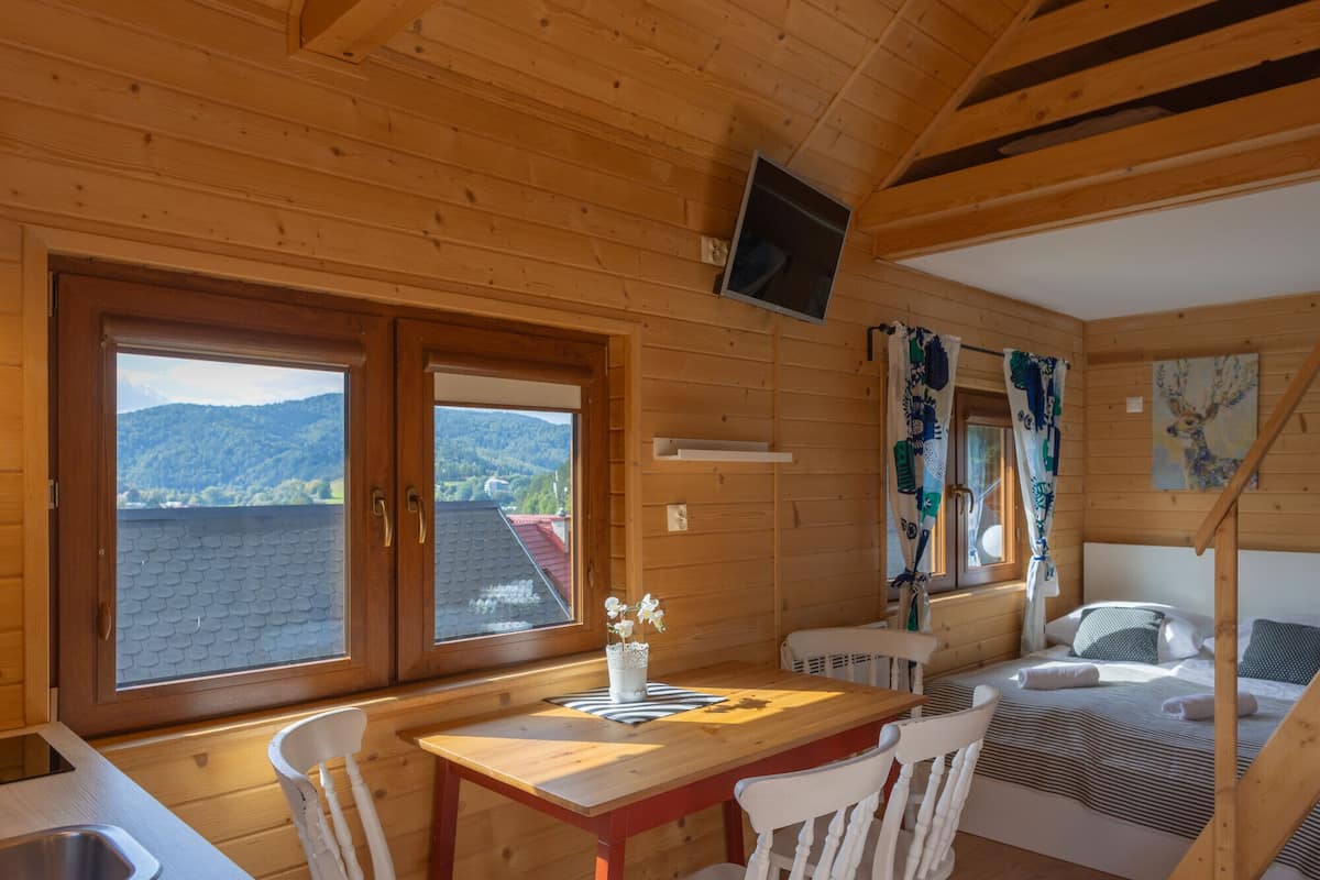 A wooden cabin with a dining area, a bed, and a TV mounted on the wall.