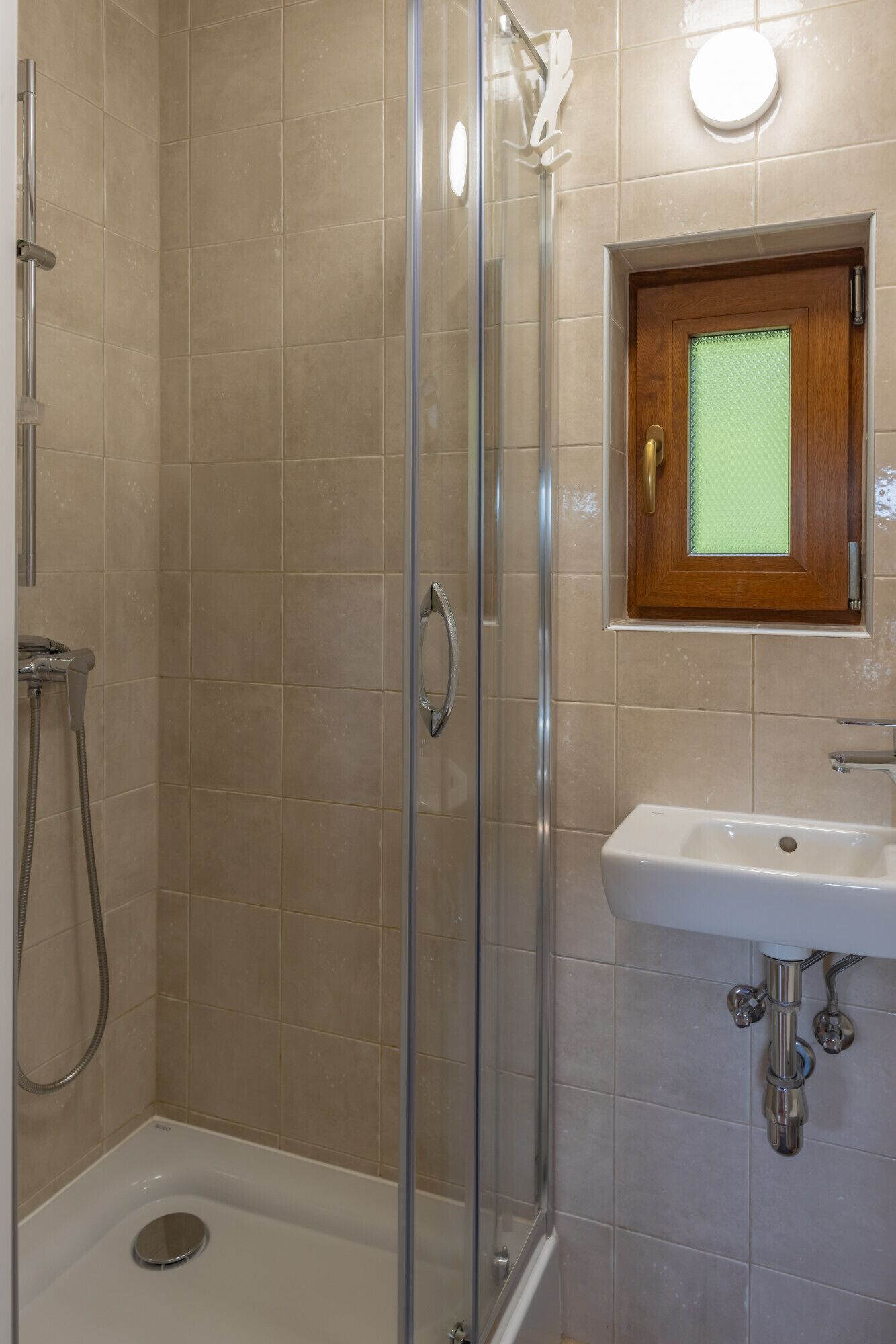 Une cabine de douche avec une porte en verre, un meuble à pharmacie en bois au-dessus du lavabo, et un lavabo blanc avec des robinets chromés.
