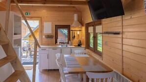 L’intérieur d’un chalet en bois comprend une cuisine, un coin repas et un téléviseur fixé au mur.