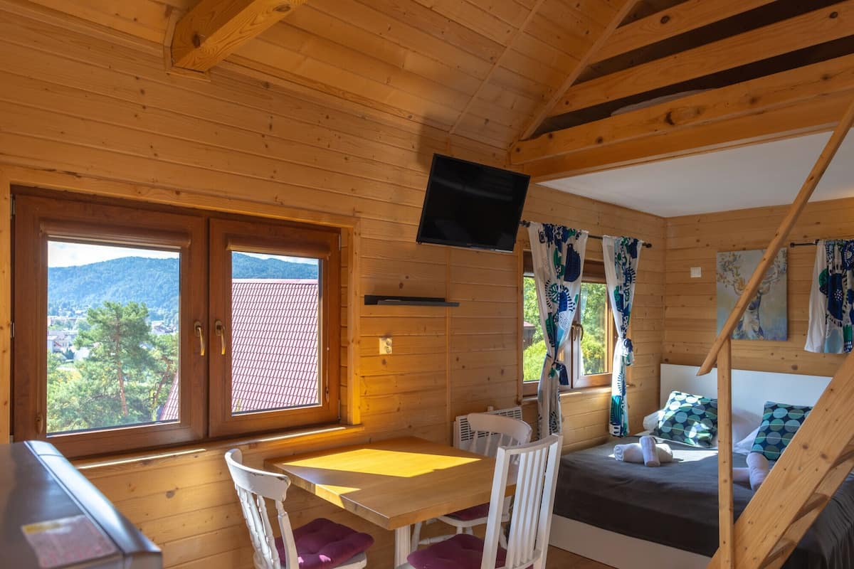 A wooden cabin with a dining area, a bed, and a TV.