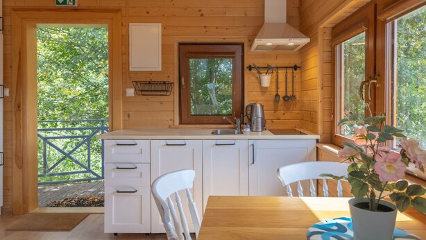 L’intérieur d’un chalet en bois comprend une cuisine, des meubles de rangement blancs, un évier et un coin repas avec une table et des chaises.