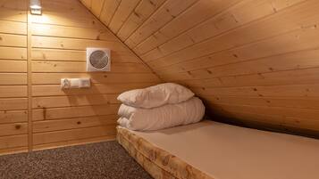 Una habitación pequeña y acogedora con techo inclinado de madera, una cama individual con ropa blanca, un aire acondicionado de pared y un enchufe.