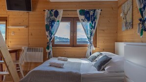 Une chambre dans un chalet en bois, avec un lit, des rideaux, une télévision et une fenêtre donnant sur un paysage agréable.