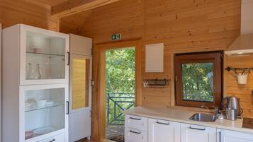 A wooden cabin interior with a kitchen area featuring cabinets, a sink, and a window overlooking greenery.