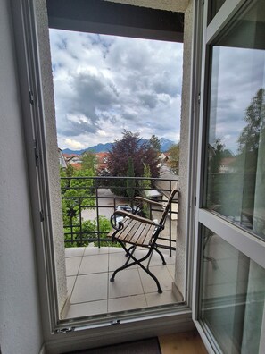 A balcony with a wooden bench, a metal railing, and a view of houses and mountains. - Garden Villa Schwanstein I Apartment "Schwanstein" (Füssen)