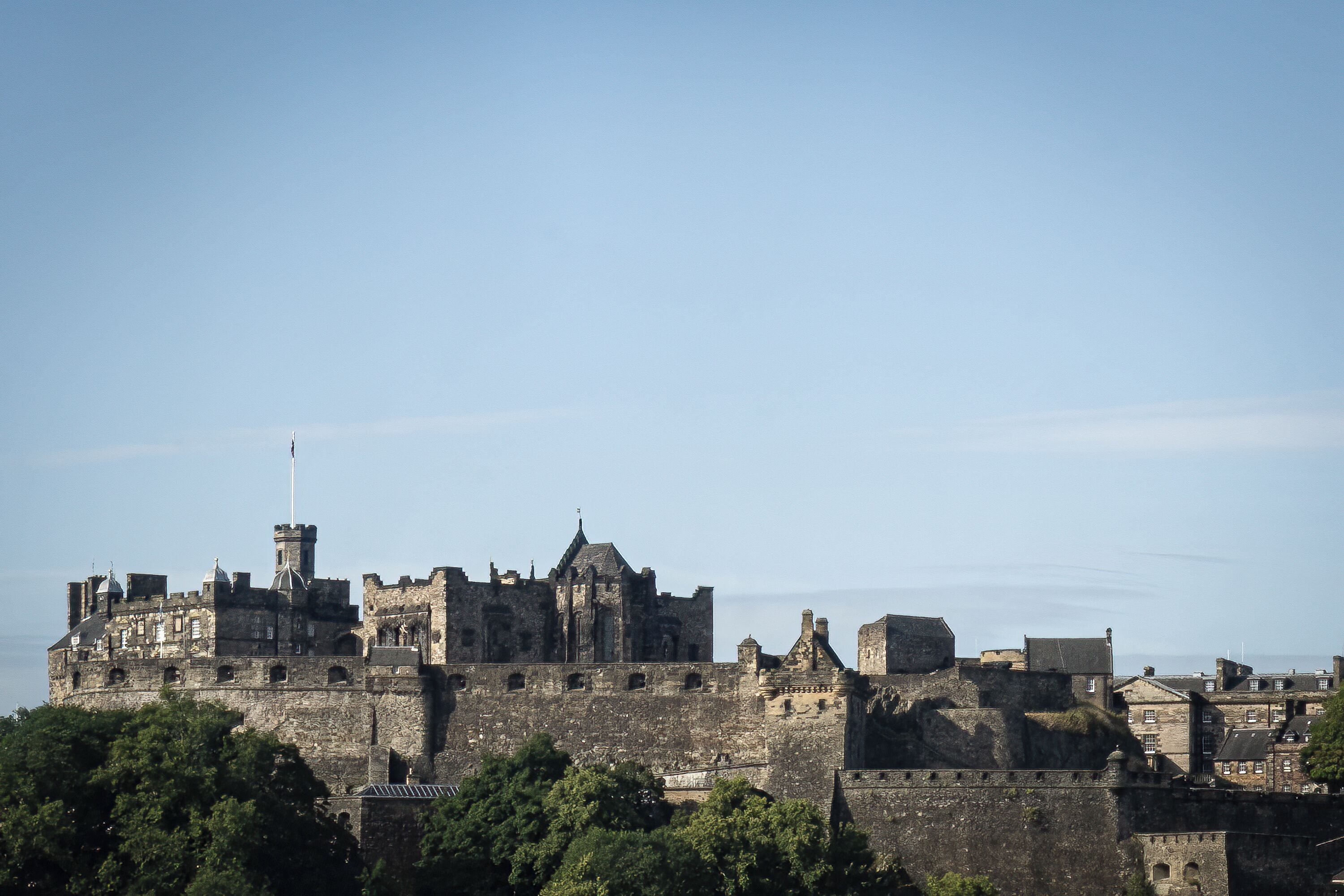 A historic stone castle with multiple towers and battlements, surrounded by greenery.