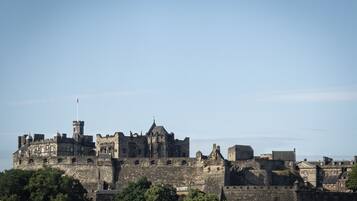 A historic stone castle with multiple towers and battlements, surrounded by greenery.