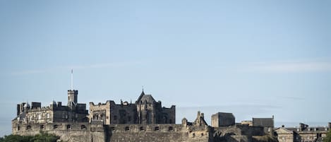 A historic stone castle with multiple towers and battlements, surrounded by greenery.
