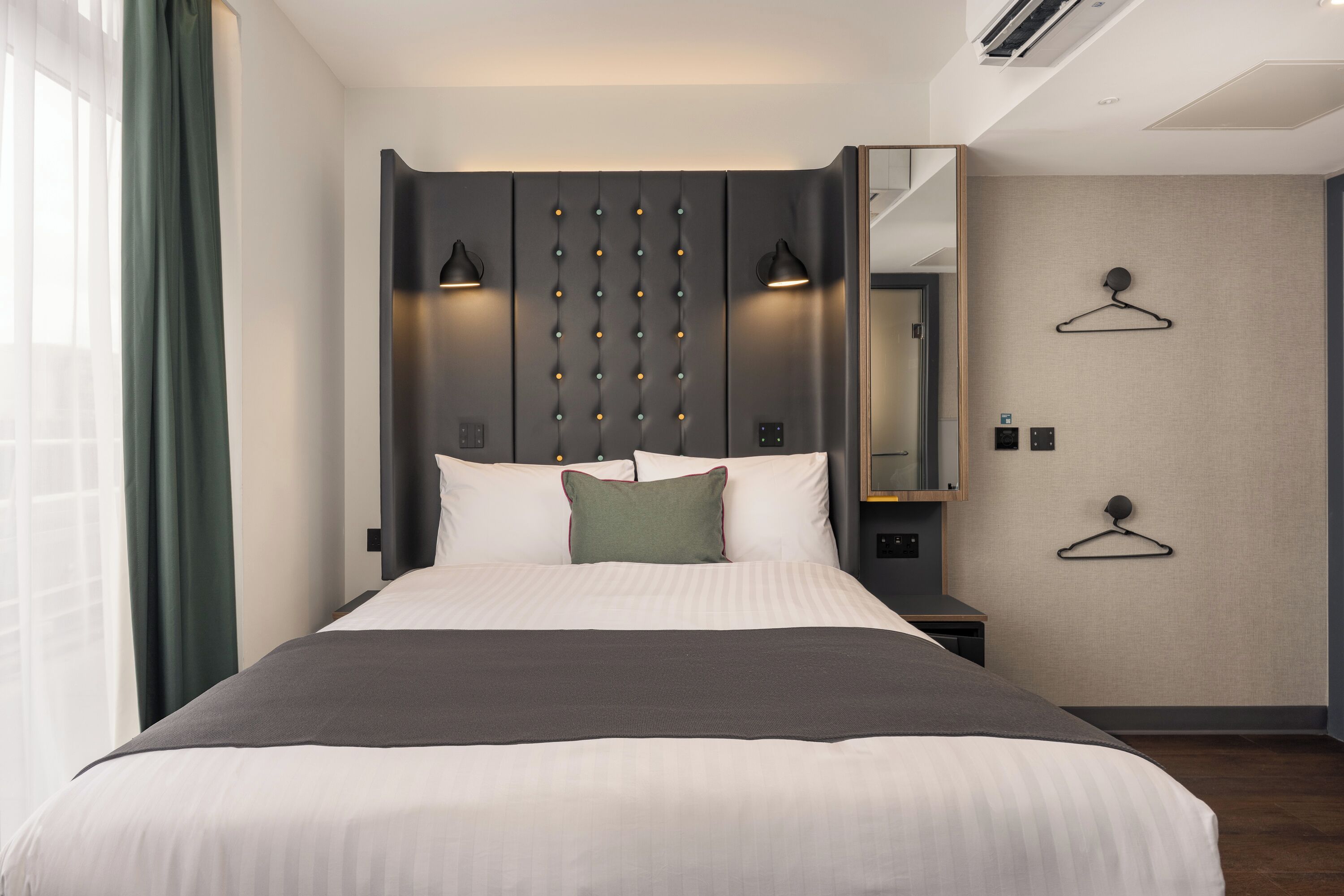 A modern hotel room with a large bed, bedside lamps, a mirror, and a wardrobe.