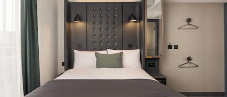 Une chambre d’hôtel moderne avec un grand lit, des lampes de chevet, un miroir et une armoire.
