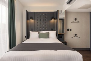 A modern hotel room with a large bed, bedside lamps, a mirror, and a wardrobe.